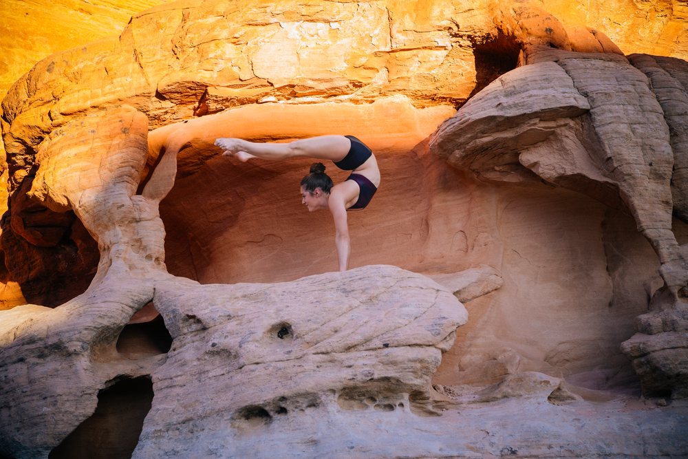Woman performing a handstand yoga pose on a rock formation in a natural outdoor landscape, USA.