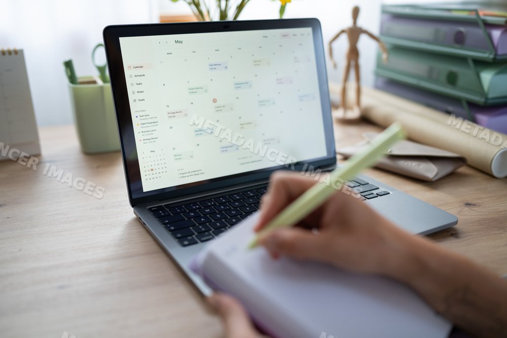 White Person planning schedule using a laptop calendar and notebook