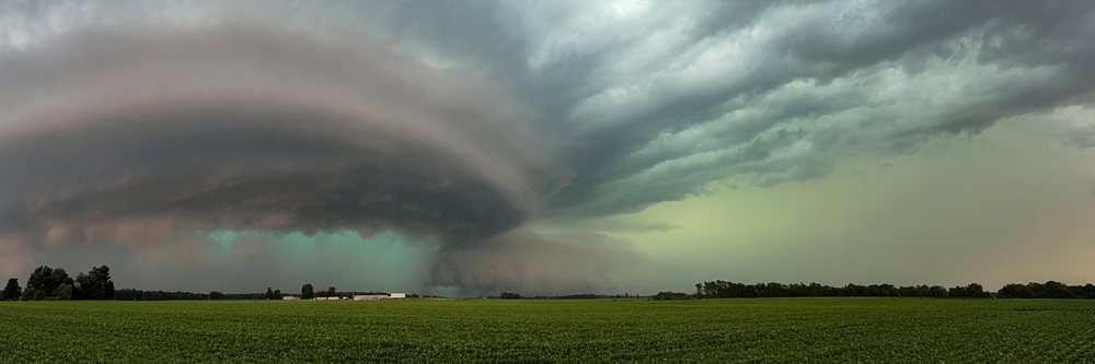 Large Supercell storm cloud with a greenish sky forms over an open rural field near farm buildings outside Charleston, linois in Tornado Alley, Weather, Environmental Issues, Storm Chasing, IL, USA.