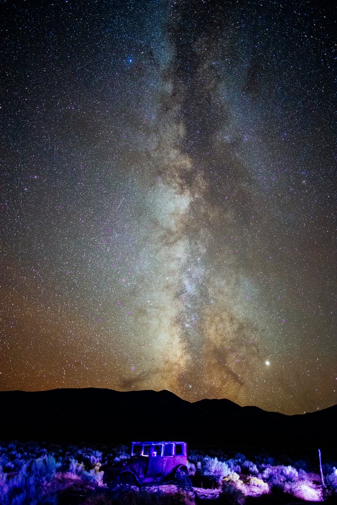 Milky Way galaxy with stars visible above a vintage car and desert scrub at night, Nevada, USA.