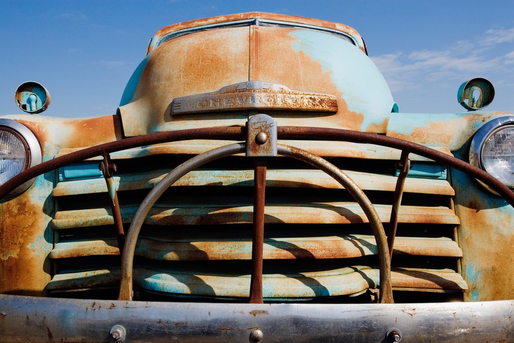 Old rusty blue Chevy pickup truck front grill with headlights and metal bumper in outdoor Texas setting, USA.