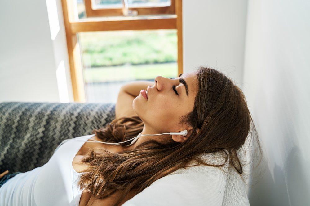A young white woman relaxes listening to music on a couch