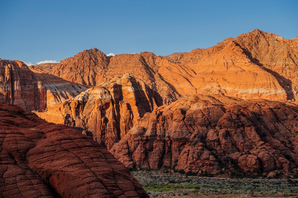 Sunrise over red cliffs and rugged rock formations in red Cliffs Desert State Park, revealing a scenic desert landscape under a clear blue sky, Snow Canyon, Utah, USA.