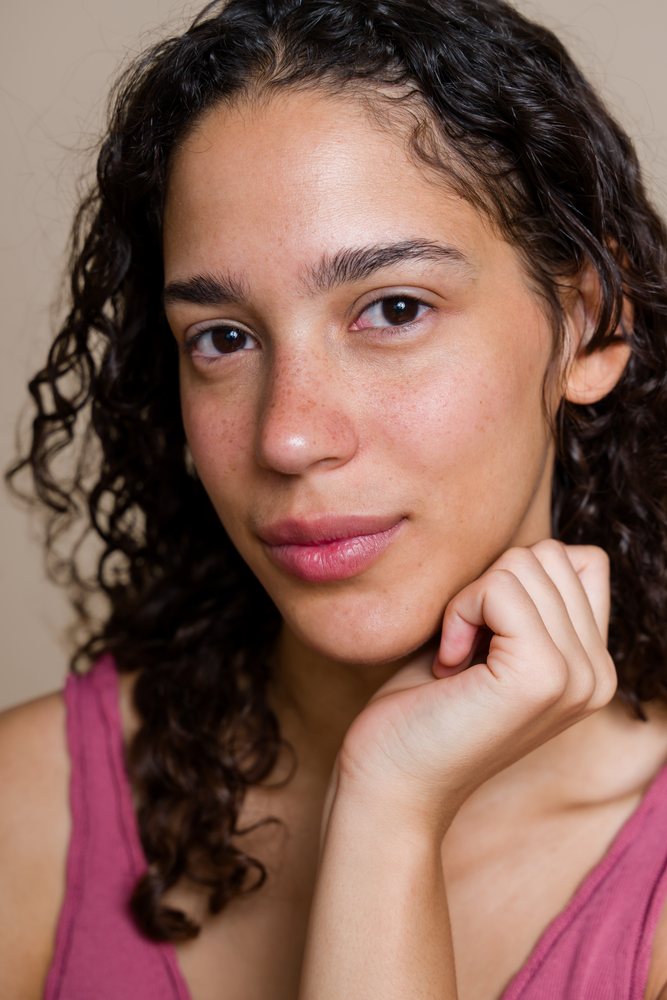 Close-up portrait of a woman with natural skin and curly hair resting her hand on her chin during a beauty shoot, Spain.