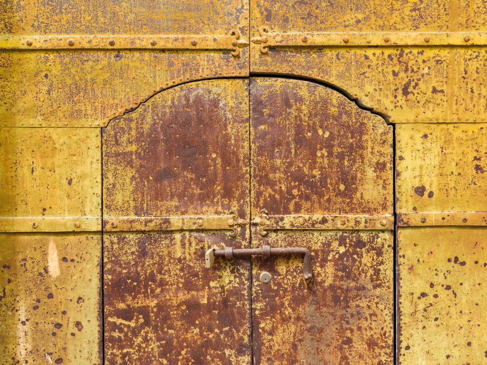 Weathered Metal Door with rusted yellow and brown metal surface and central lock, Pisticci, Basilicata, Italy.