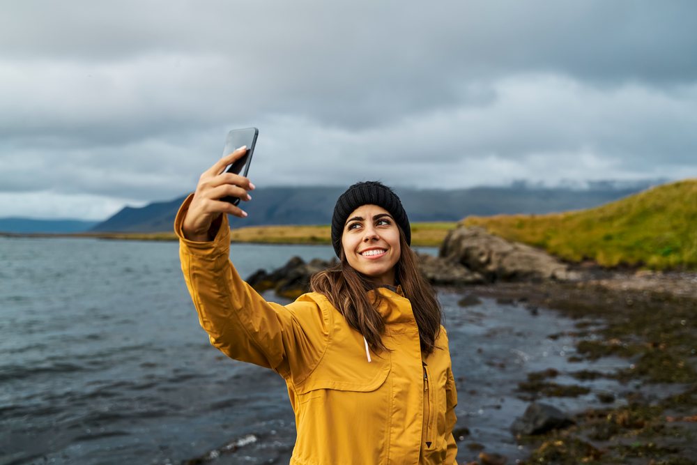 Young white woman takes selfie at rocky shoreline in Iceland