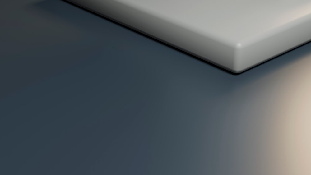 Smooth rectangular object with rounded corners casts a shadow on a grey surface in a minimalist setting with soft lighting.