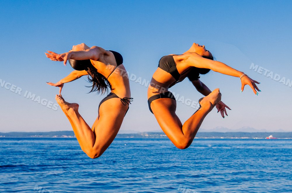 Two women performing partner acrobatics leap over ocean in washington