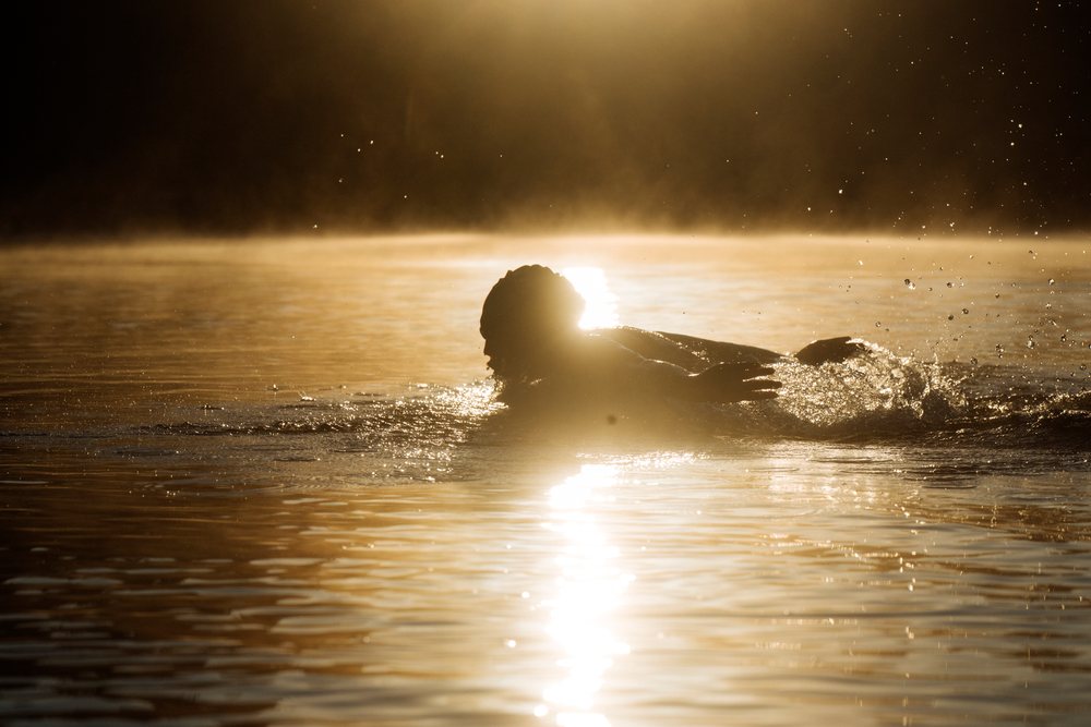 Swimmer performing a swimming stroke in open water during early morning with sunlight reflecting off the water surface, USA.