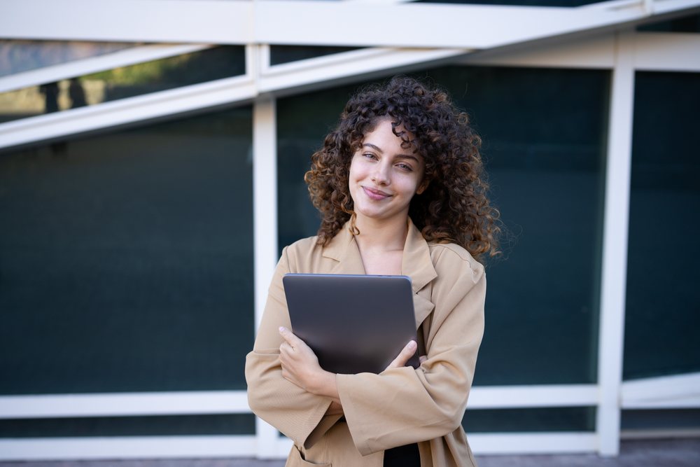 Woman with curly hair holding a tablet standing outside a modern building, Spain.