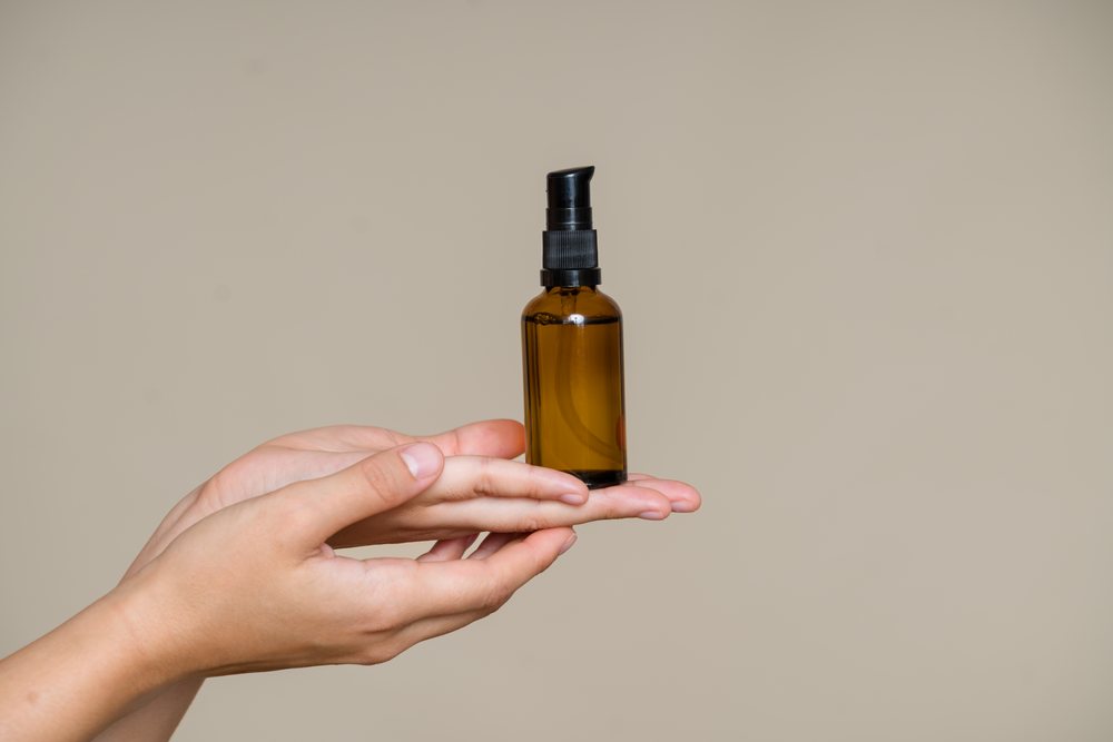 Human hand holds an amber glass bottle with a black pump dispenser against a neutral background, beauty shoot, Spain.