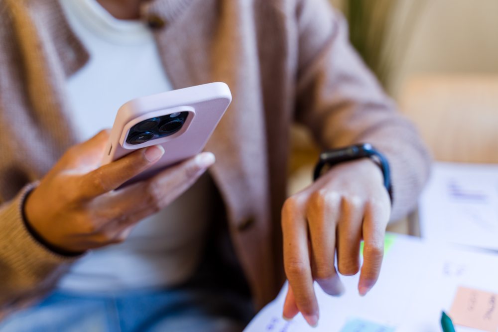 Person holding a mobile phone and pointing at paper documents at a workspace, Spain.