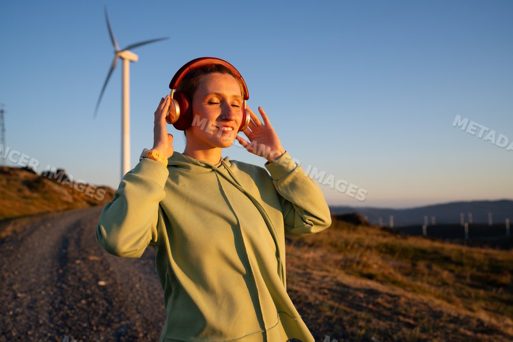 White Woman enjoying music outdoors near a wind turbine at sunset