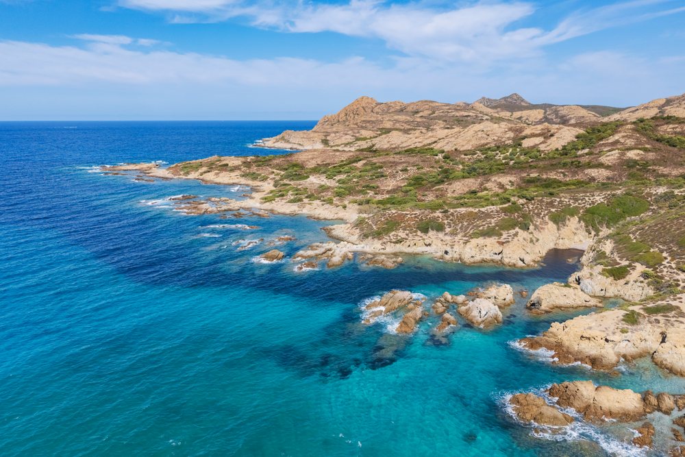 Rocky coastline along the clear turquoise Mediterranean Sea at Plage de l'Ostriconi, France under a blue sky, Travel Photography, Ile Rousse, Corsica.