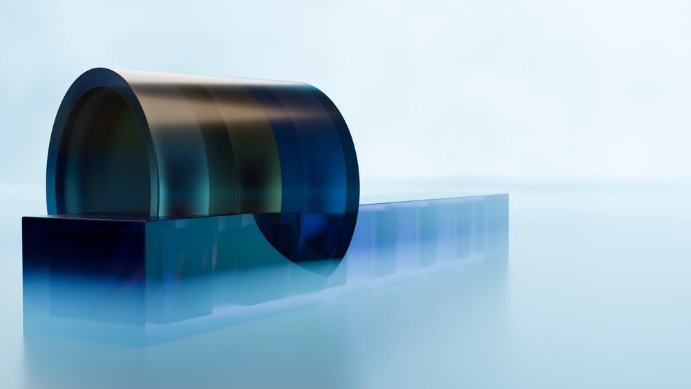 Blue glass sculpture with a curved glass form placed atop a translucent rectangular block in a minimalist studio setting.