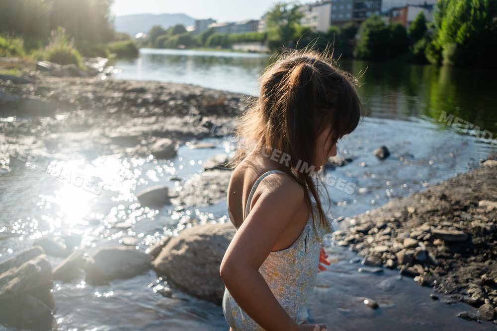 A young white girl playing by the rocky riverbank