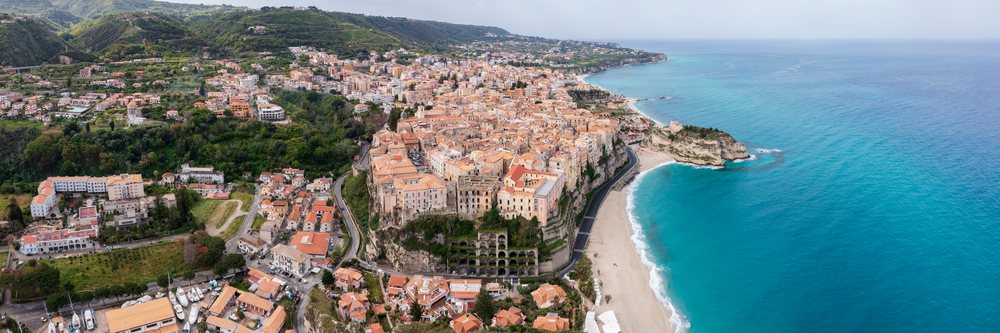 Coastal town of Tropea perched on cliffs overlooking the Mediterranean Sea with sandy beach, green hills, and marina, Calabria, Italy.