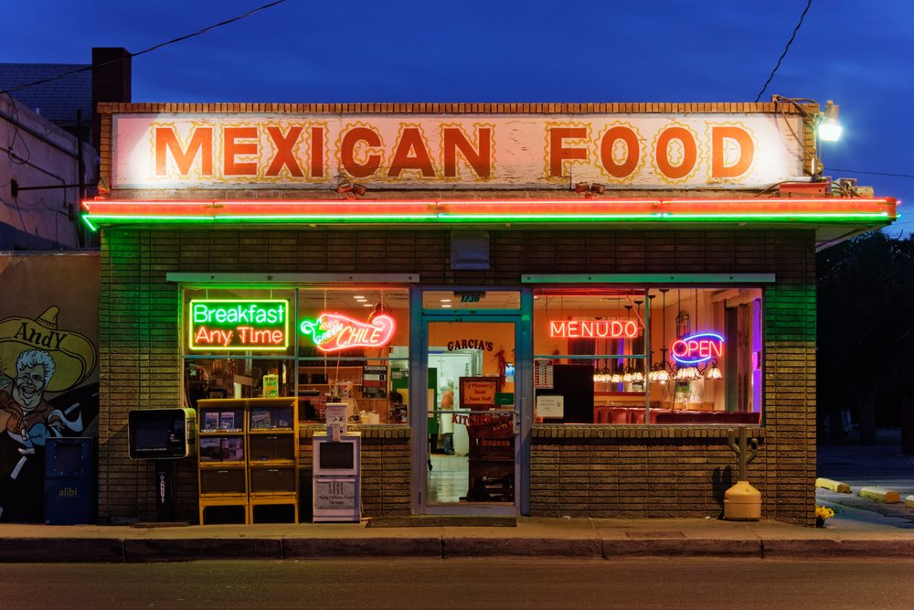 Mexican restaurant with neon signs for breakfast, chile, and menudo on a brick street building at night, New Mexico, USA.