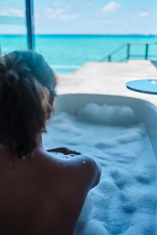 A woman enjoying a relaxing bubble bath with a turquoise ocean view in the, Maldives.