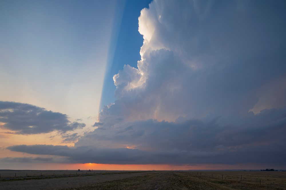 Large storm cloud with illuminated edges and crepuscular rays visible over a flat rural landscape at sunset, Storm Chasing, Weather, Environment, Grover, Colorado, USA.