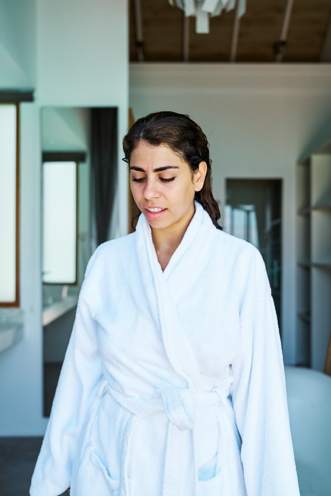 A woman wearing a white bathrobe relaxes indoors inside a modern home in the, Maldives.