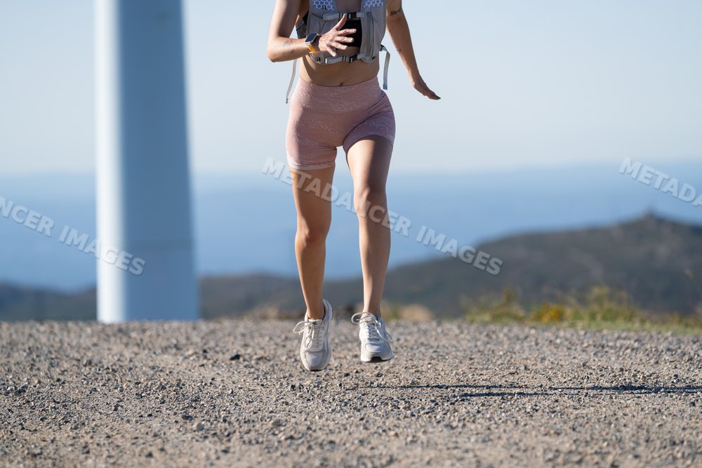 White Woman running on a trail near a wind turbine in Galicia, Spain