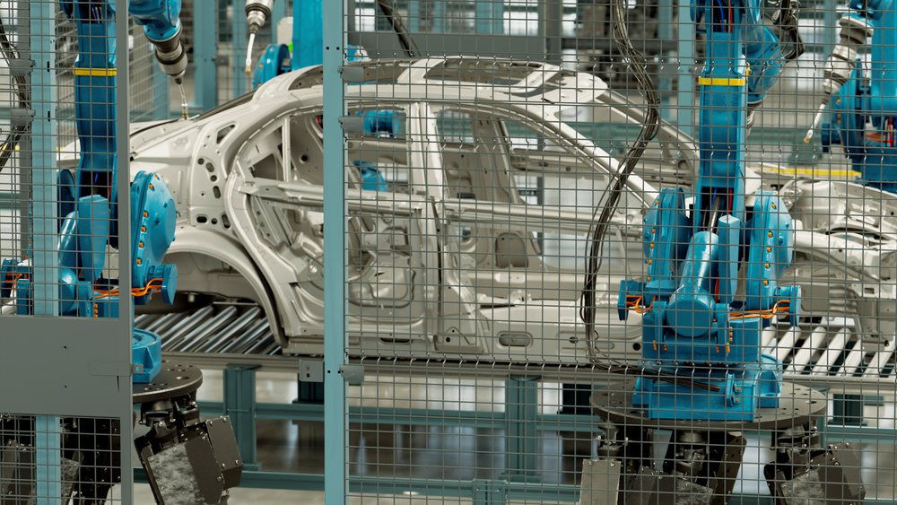 Blue robotic arms operate on metal car body frames along an assembly line in an industrial manufacturing factory.