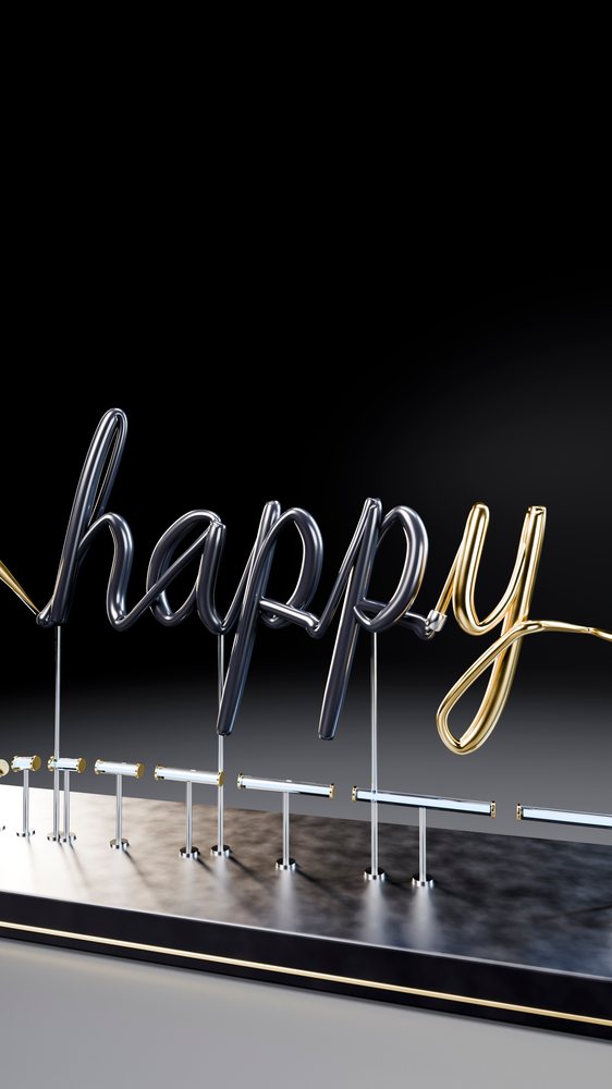Metal sculpture spelling 'happy' in silver and gold on a black base against a dark background.