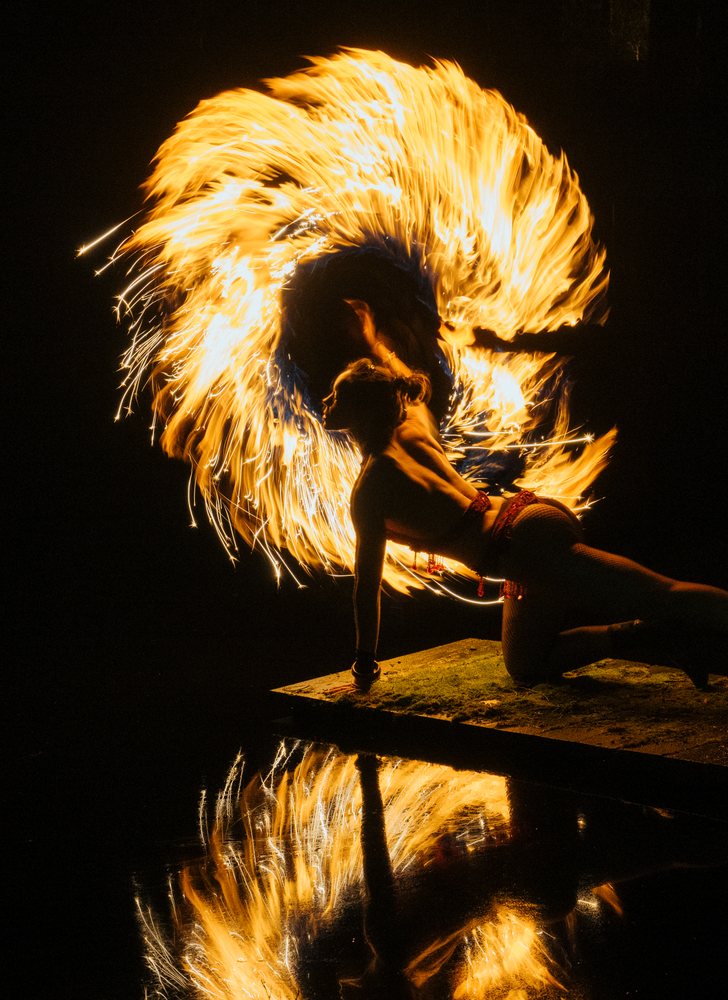 Woman fire dancer performs a spinning fire act at night, creating vivid flame reflections on water, artistry, artist, USA.