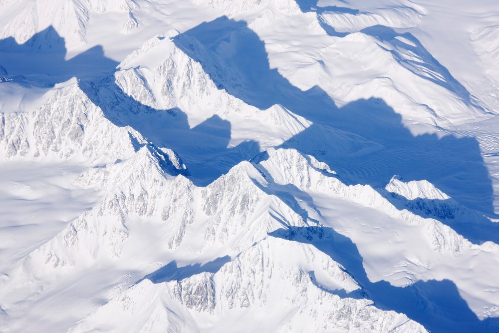 Snow-covered mountain peaks and ridges cast shadows across Alaska's frozen wilderness landscape.
