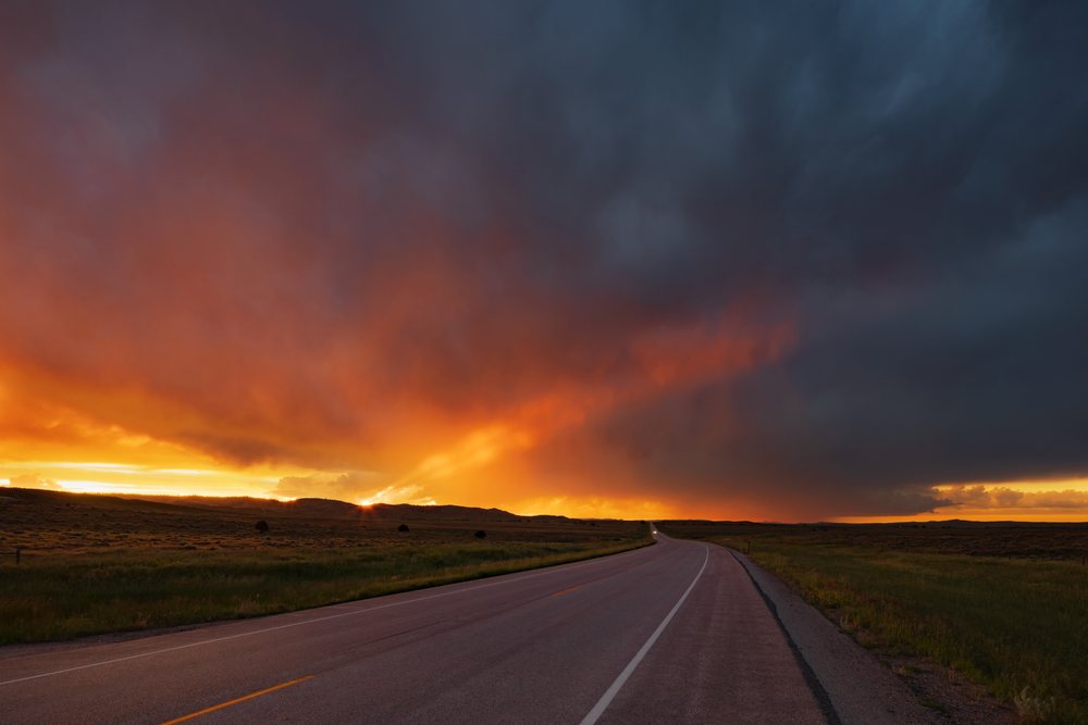 Sunset with dramatic storm clouds over highway 59 north of Gillette, in an open rural landscape with grass fields, Wyoming, USA.