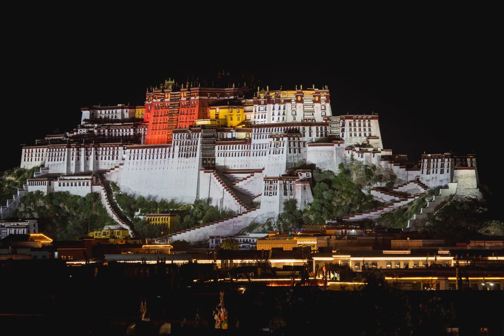 Potala Palace illuminated at night on a hilltop, Tibet, showing its architectural grandeur with city lights below, Lhasa, Autonomous Region of Tibet.