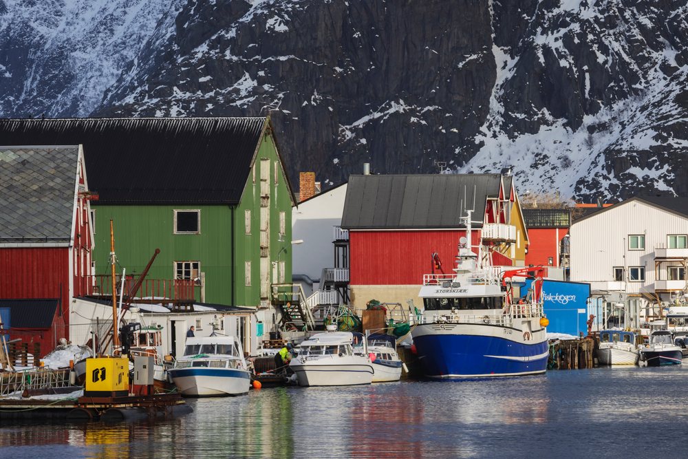 Fishing boats moored at Henningsvaer port with colorful buildings and snow-covered mountains, Landscape, Lofoten, Norway.