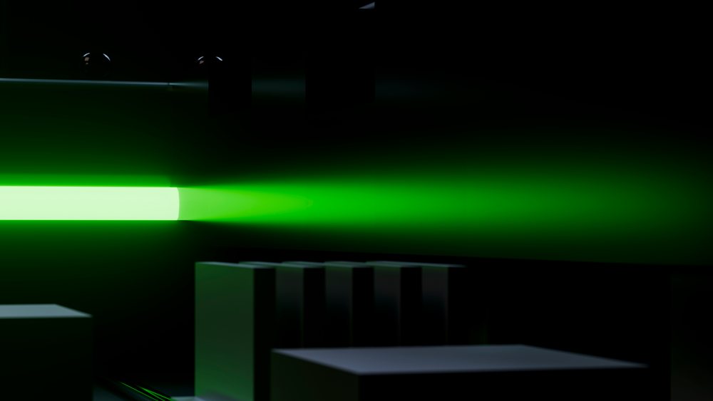 Green laser beam glows and scatters light in a dark room with a black background.