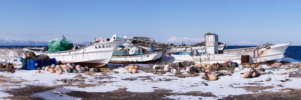 Fishing boats with ropes and buoys on snow-covered ground by the sea in winter, Shiretoko Peninsula, Hokkaido, Japan.