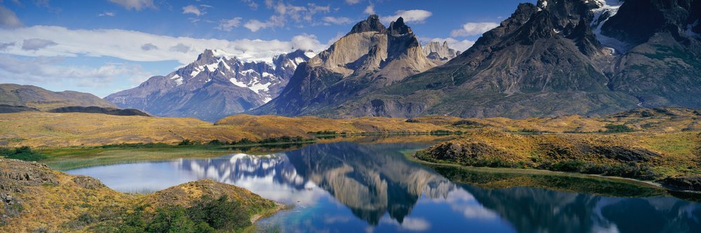 Los Cuernos mountains with rocky peaks reflect over a calm lake under a blue sky, Torres del Paine National Park, Chile.