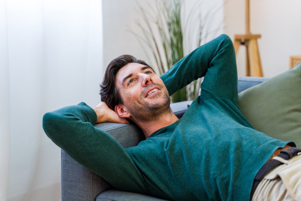 Man reclining on a gray couch wearing a green sweater in a cozy living room, Spain.