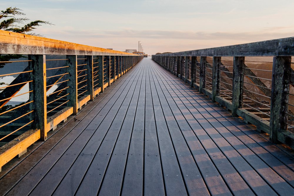Wooden boardwalk with railings extends into the sunset under an evening sky with trees to the left, northern, Oregon, California, USA.