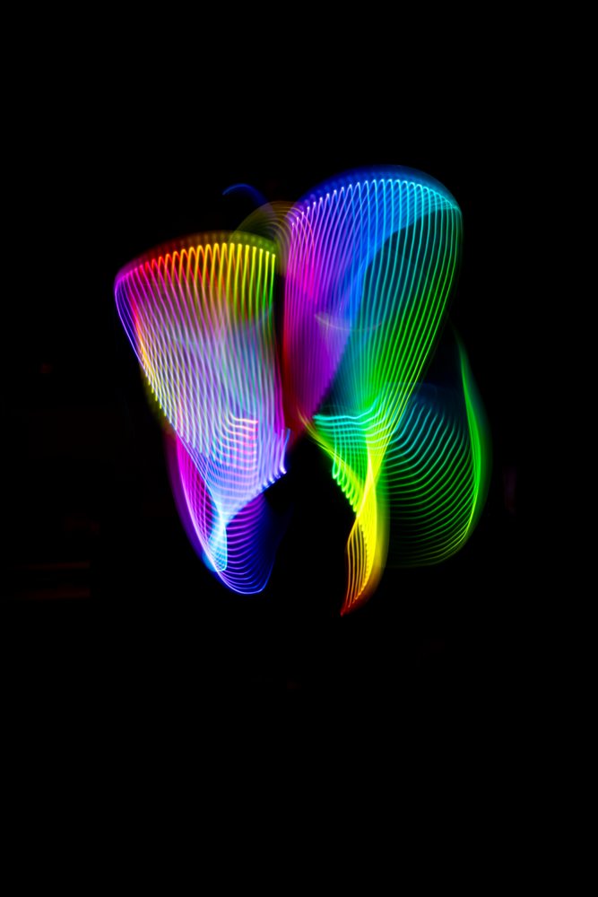 Colorful LED light painting showing vibrant wave-like rainbow light trails on a dark background.