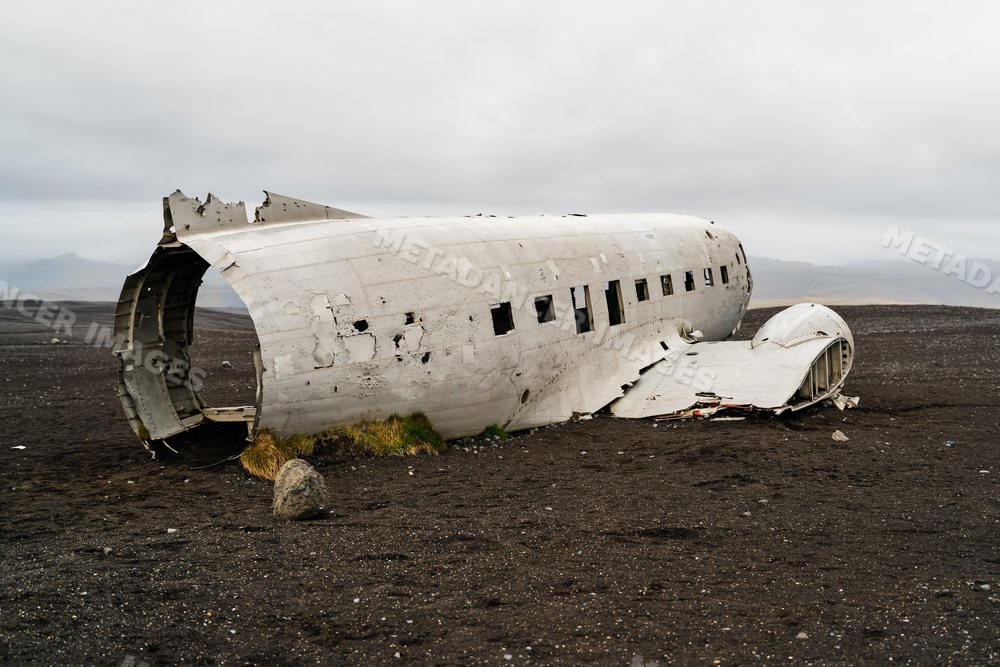 A wrecked airplane fuselage lies abandoned on black sand