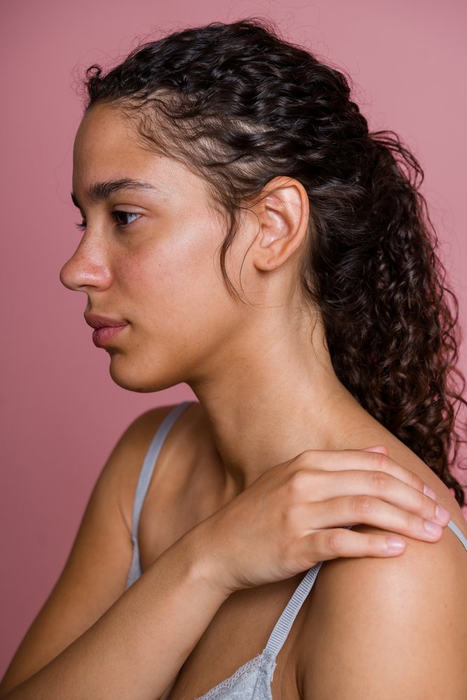 Young woman with curly hair in profile touches her shoulder against a pink background during a beauty shoot, Spain.