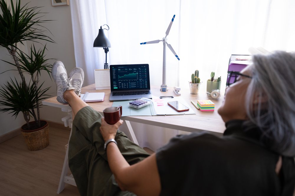 Senior woman relaxing in a bright home office with laptop and wind turbine model, Spain.