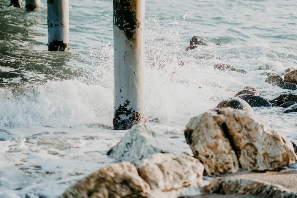 Waves crash against pier pillars and rocks on the shore, producing sea foam and splashes at the seashore, Spain.