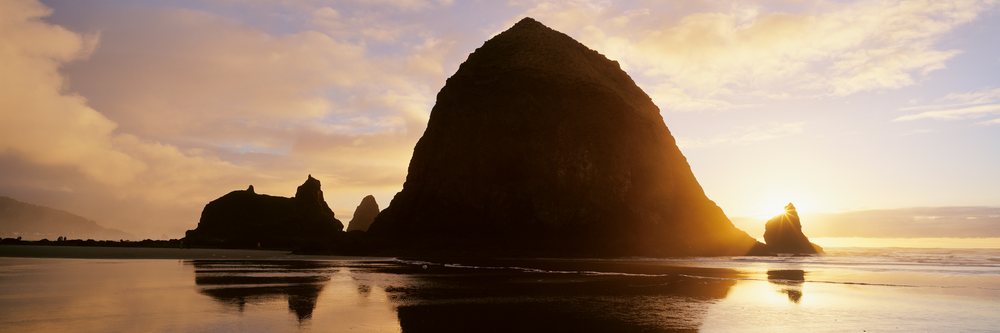 Silhouetted Haystack Rock at sunset reflecting on the wet sandy beach at Cannon Beach, Oregon, USA.