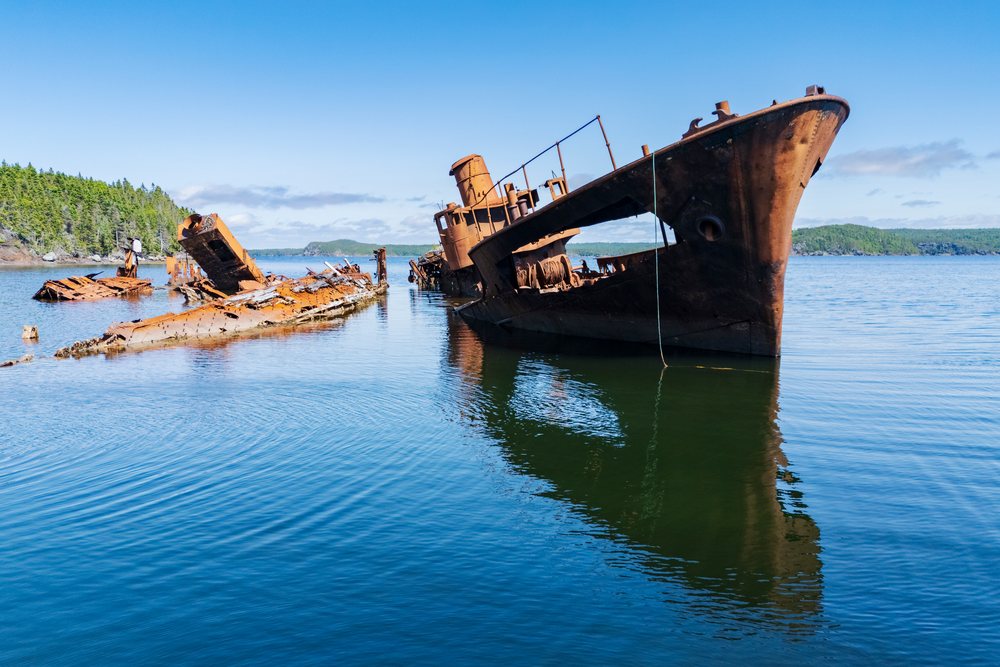 Rusted wreck of HMS Calypso protrudes from the water, Canada under a clear blue sky with reflection on the water, Landscape, Wildlife, Lifestyle, Embree, Newfoundland & Labrador.