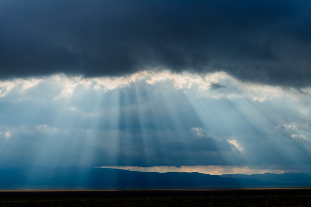Sun rays break through dramatic clouds over mountains and open land, Nevada, USA.