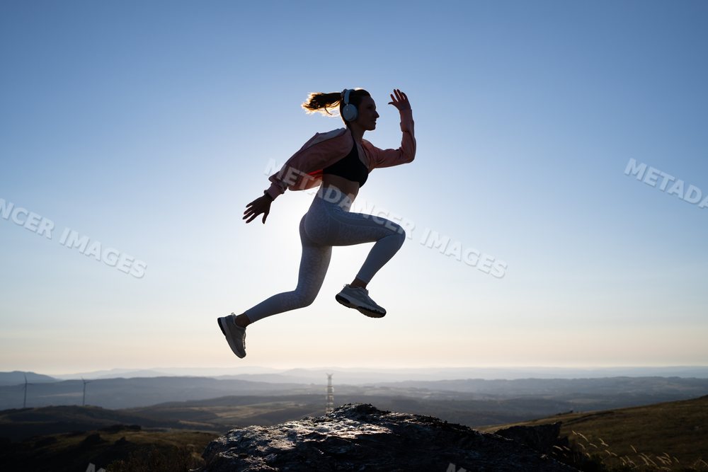 A white woman jumps energetically outdoors on a rocky hill in Galicia