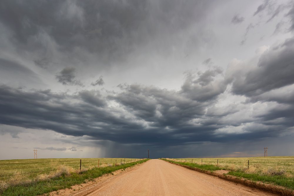 Dark storm clouds forming a Supercell over a dirt road through grassland, Cheyenne, Wyoming, USA.