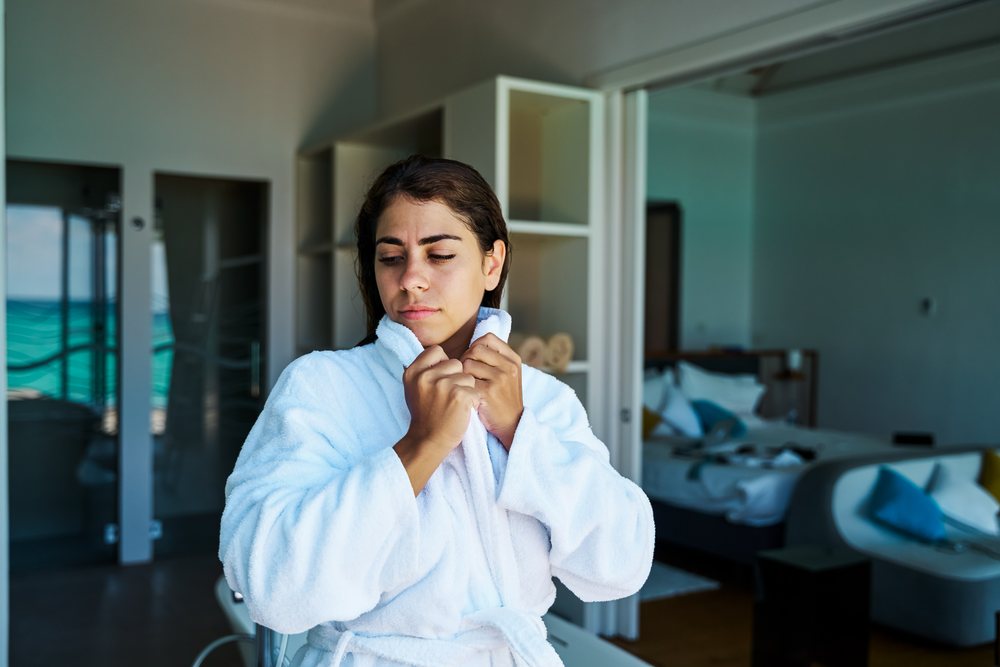 A woman wearing a white bathrobe relaxes in a modern hotel room with a view of the sea in the, Maldives.