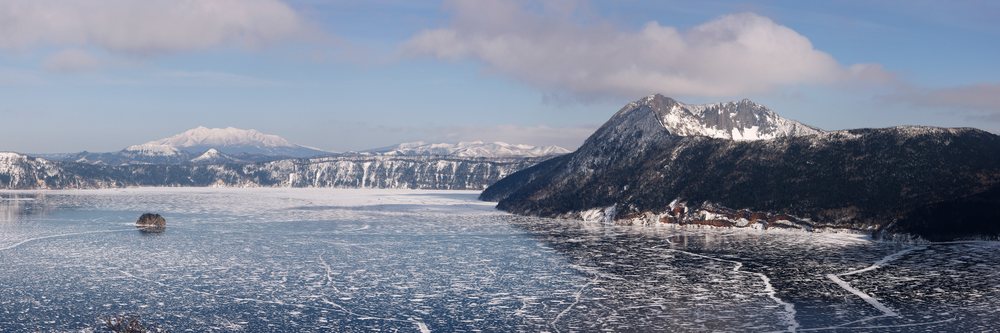 Lake Mashu is frozen with visible ice cracks and snow-covered mountains, Hokkaido, Japan.